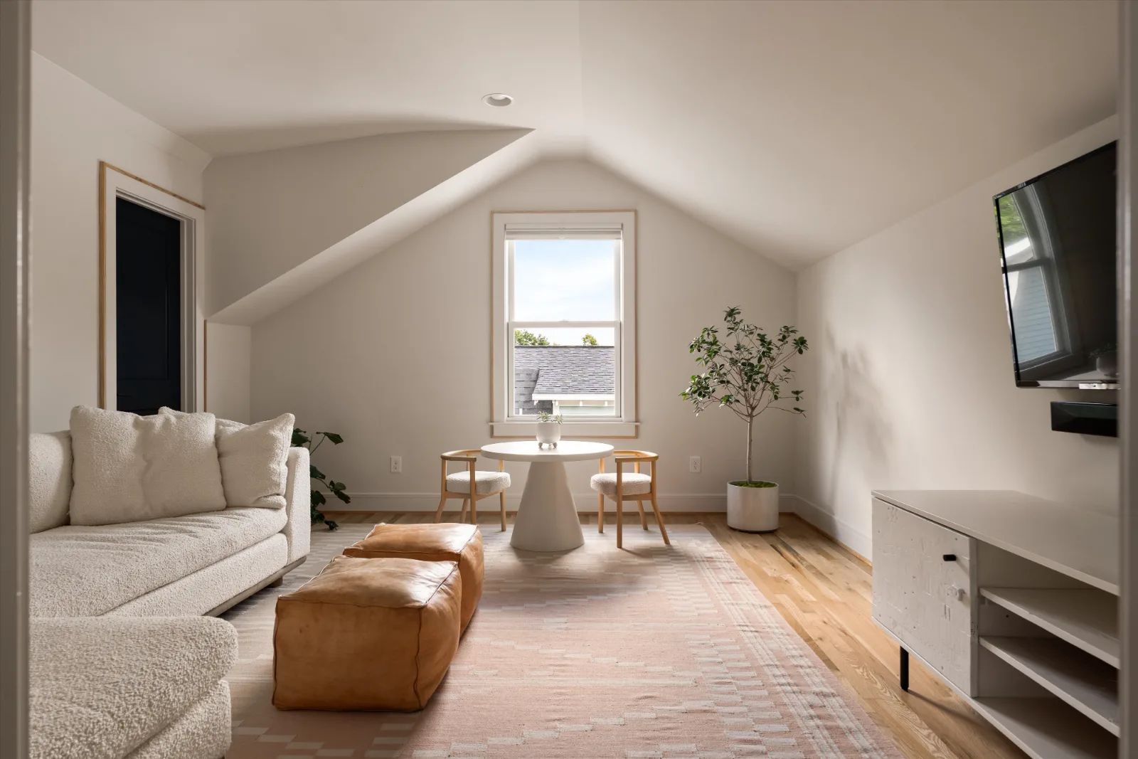 The upstairs bonus room: vaulted ceiling, a sofa, a small table by the window and a wall for the television