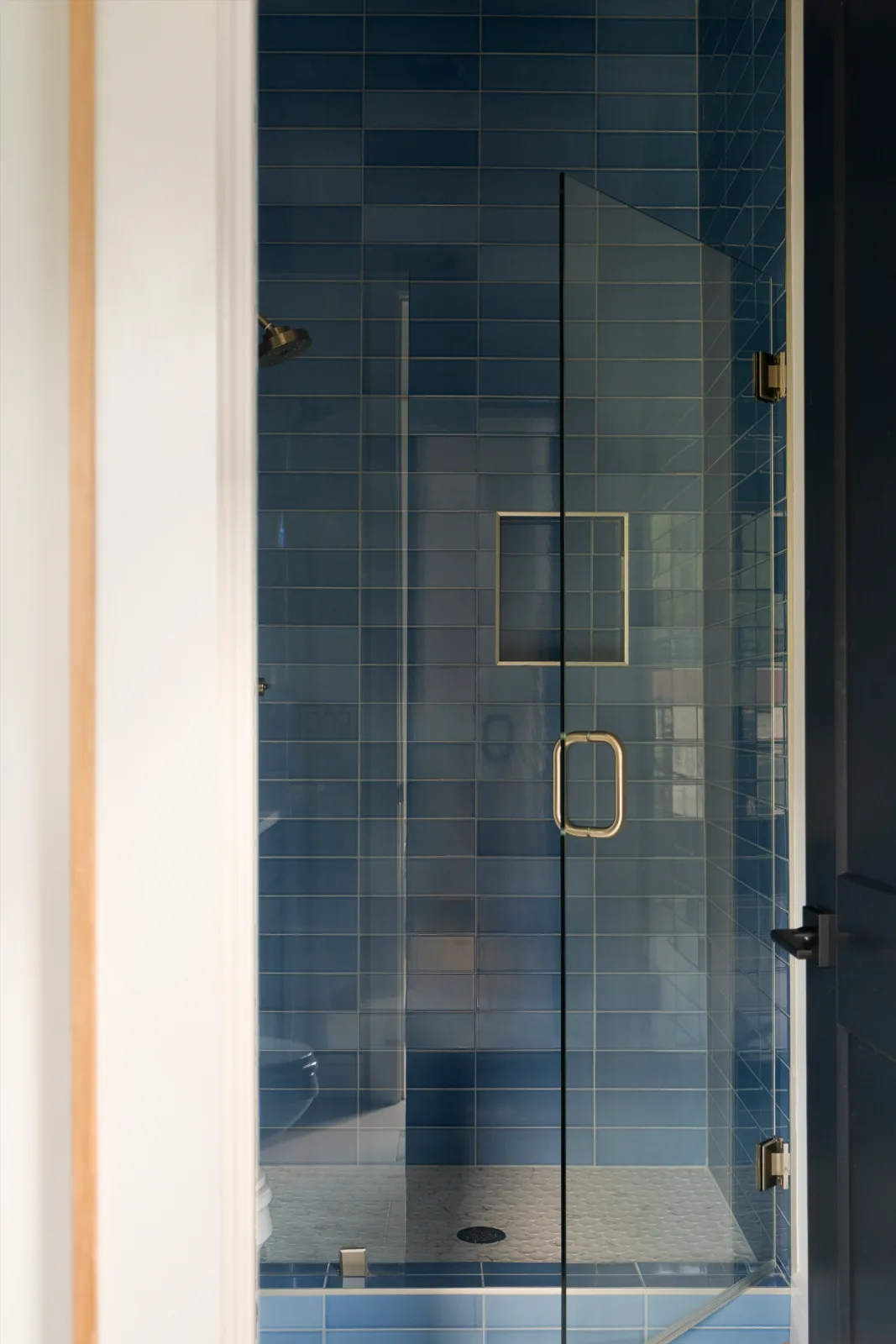 The en-suite bath through the doorway: blue tile to the ceiling, glass shower door and brass fittings