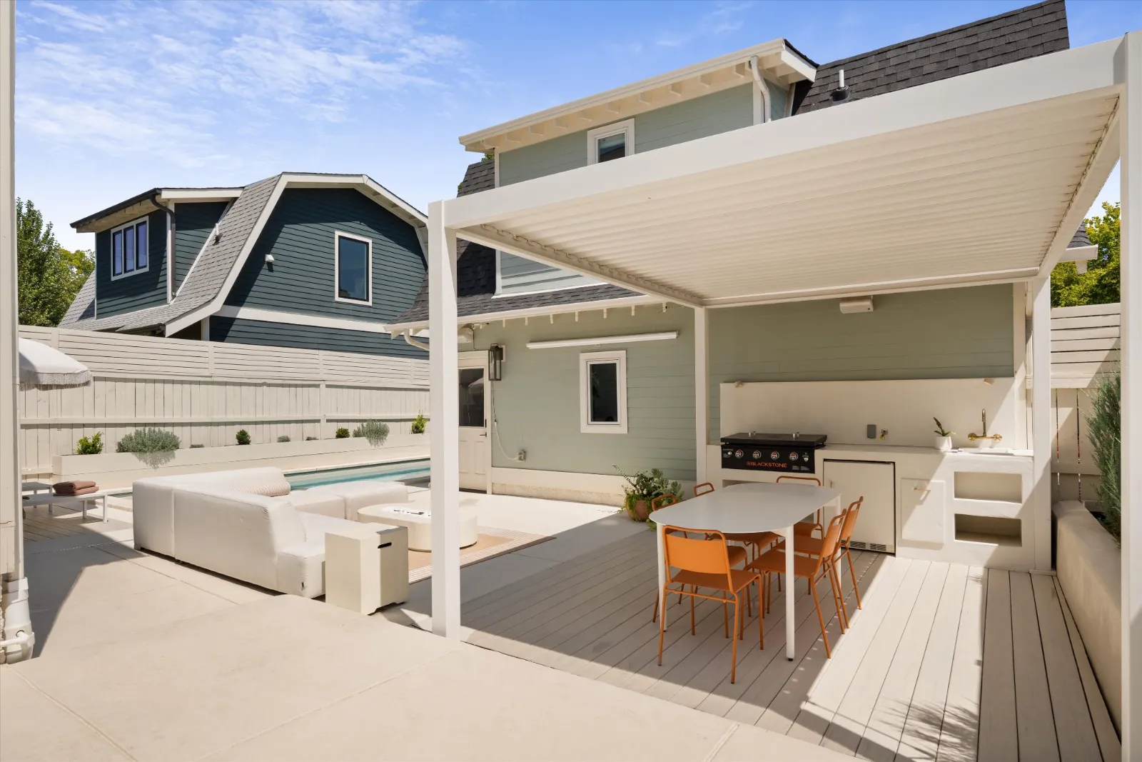 The courtyard behind the house: louvered pergola over the outdoor kitchen and dining table, the saltwater pool beyond, and the guest house at the rear