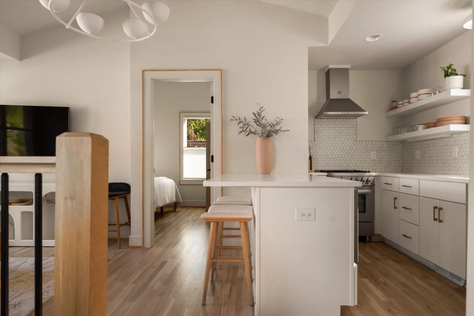 The island with two stools, the kitchen beyond and the bedroom through the doorway