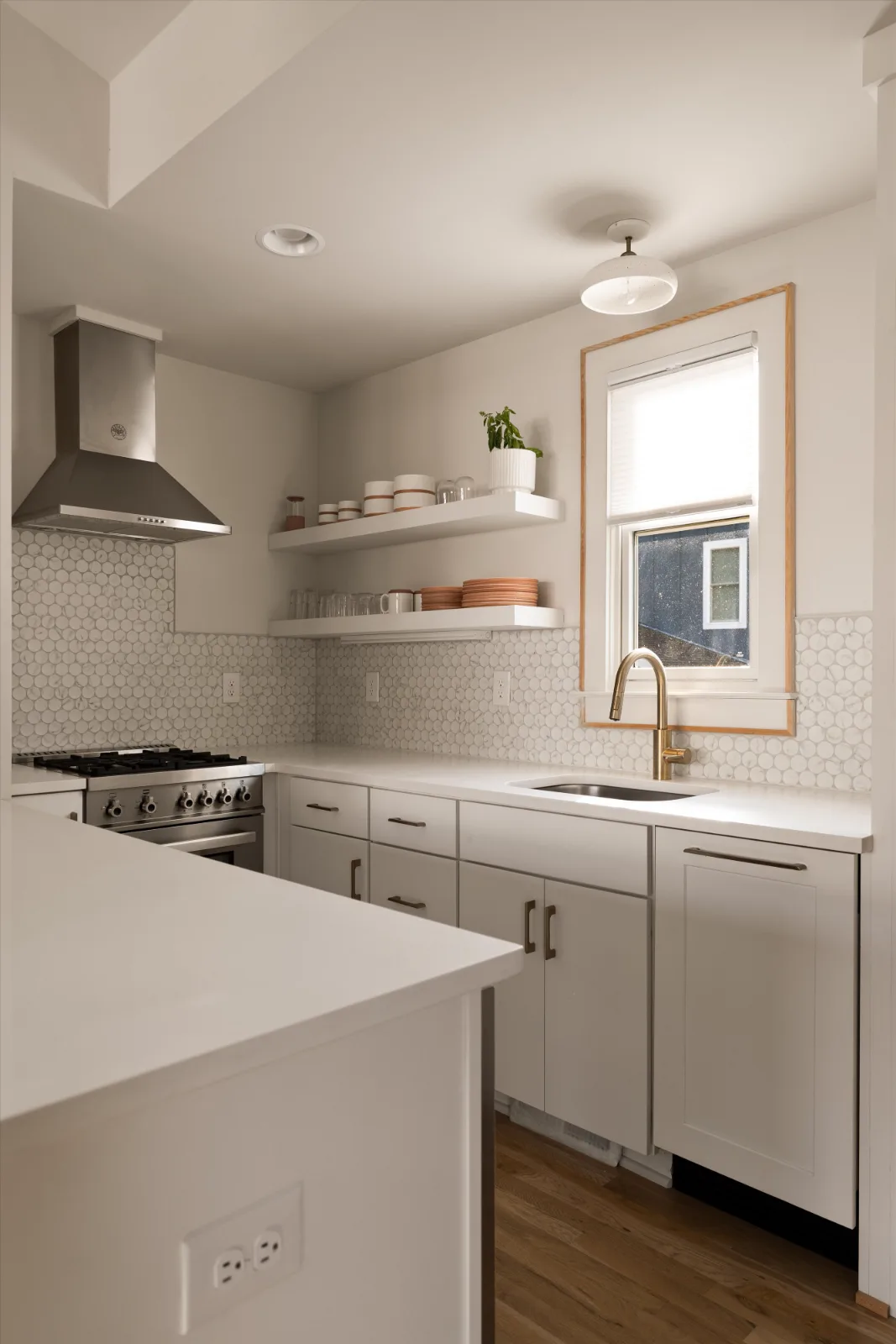 The guest suite kitchen: gas range under a stainless hood, penny tile, open shelving and a brass tap