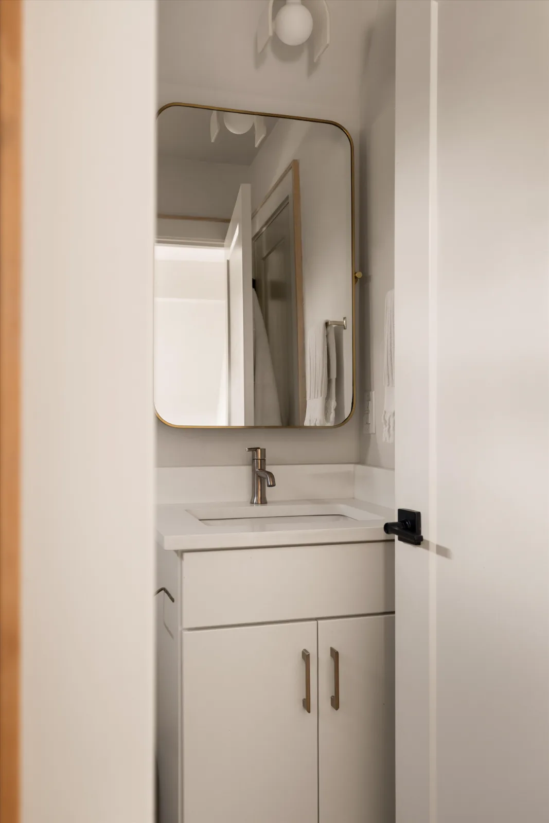 Looking through the door to the vanity, brass-framed mirror and sconce above