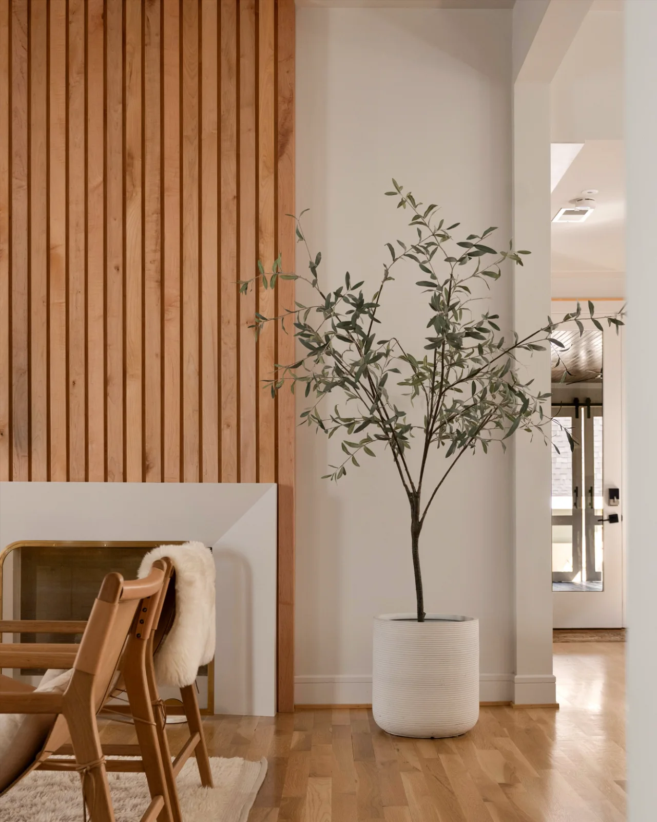The white oak slat wall above the firebox with its brass surround, seen from the hall