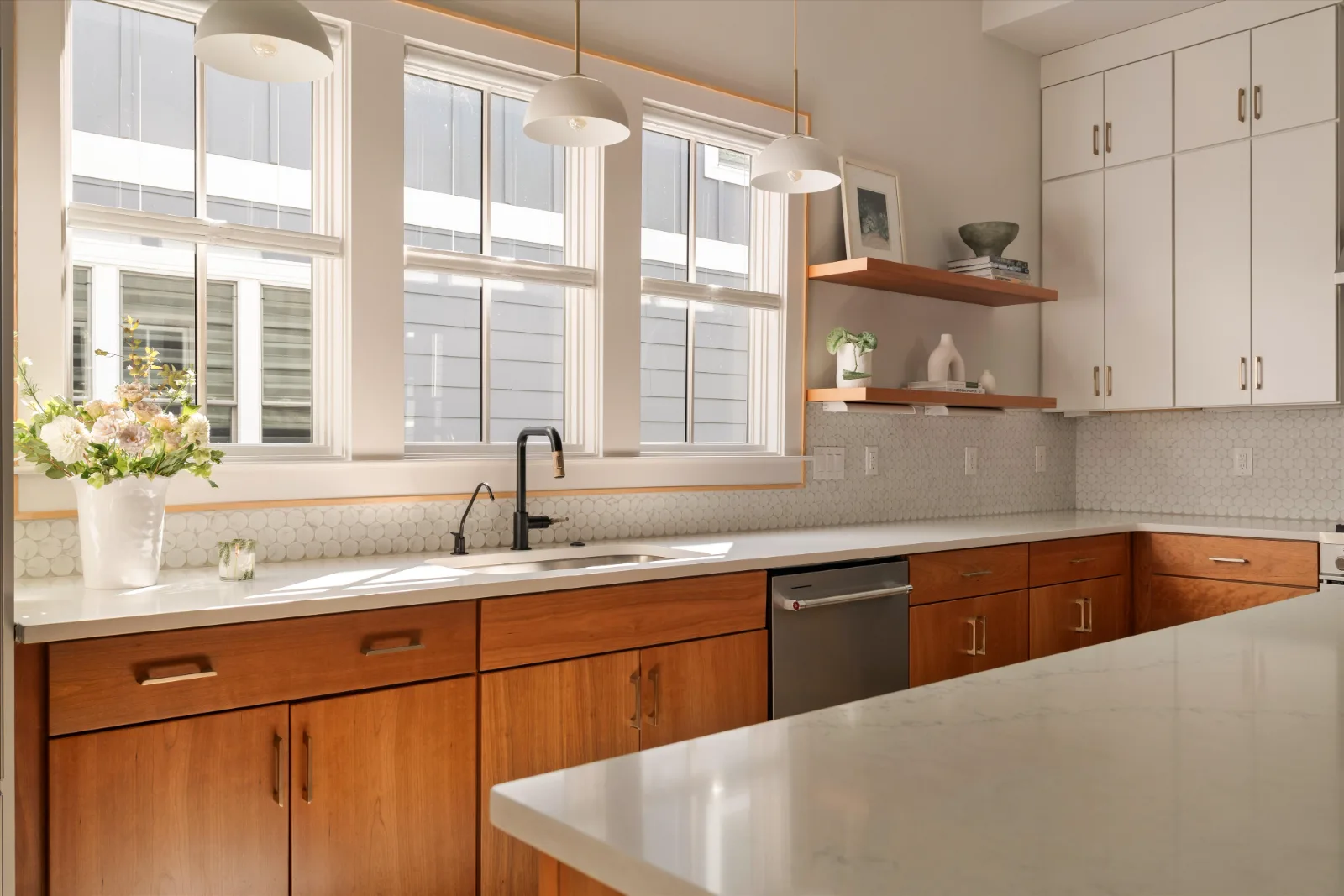 The sink wall under three tall windows, floating cherry shelves alongside