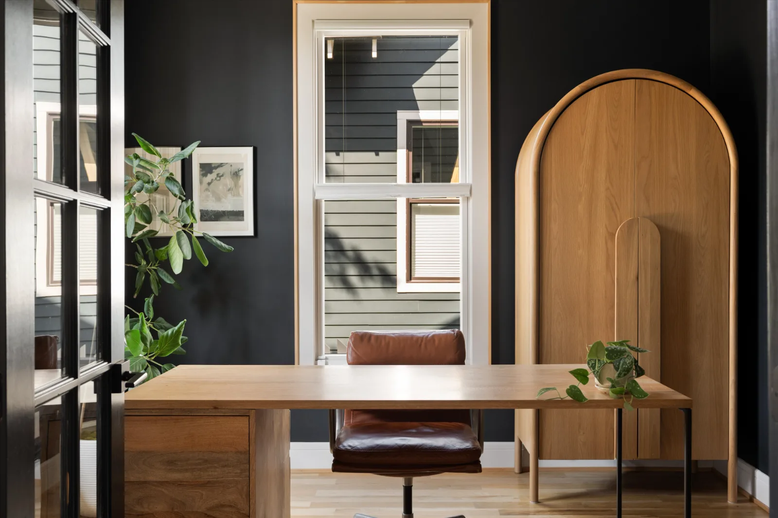 The office behind glass French doors: a white oak desk, arched cabinet and black walls