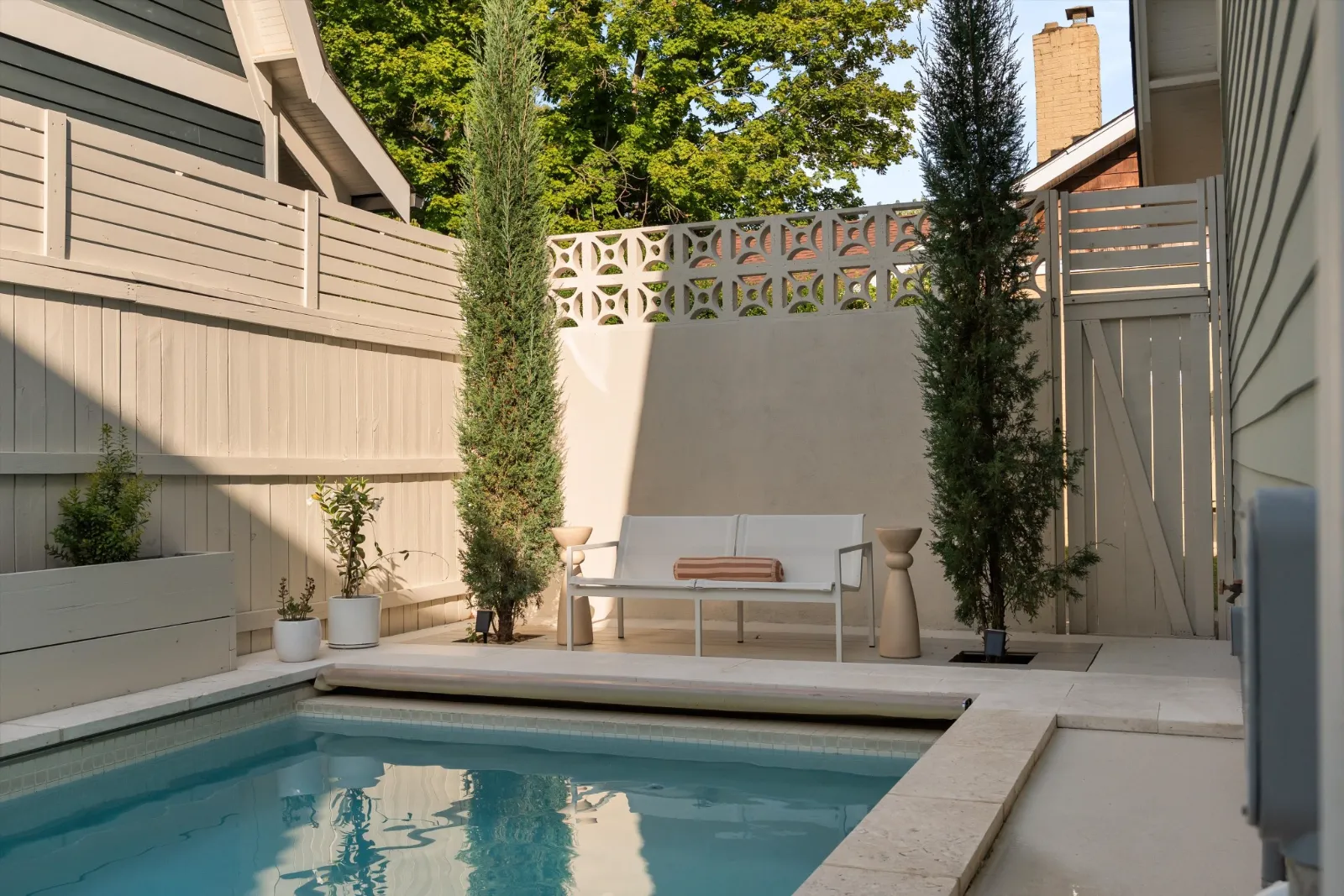 The saltwater pool with travertine coping, a bench against the stucco garden wall and cypresses either side