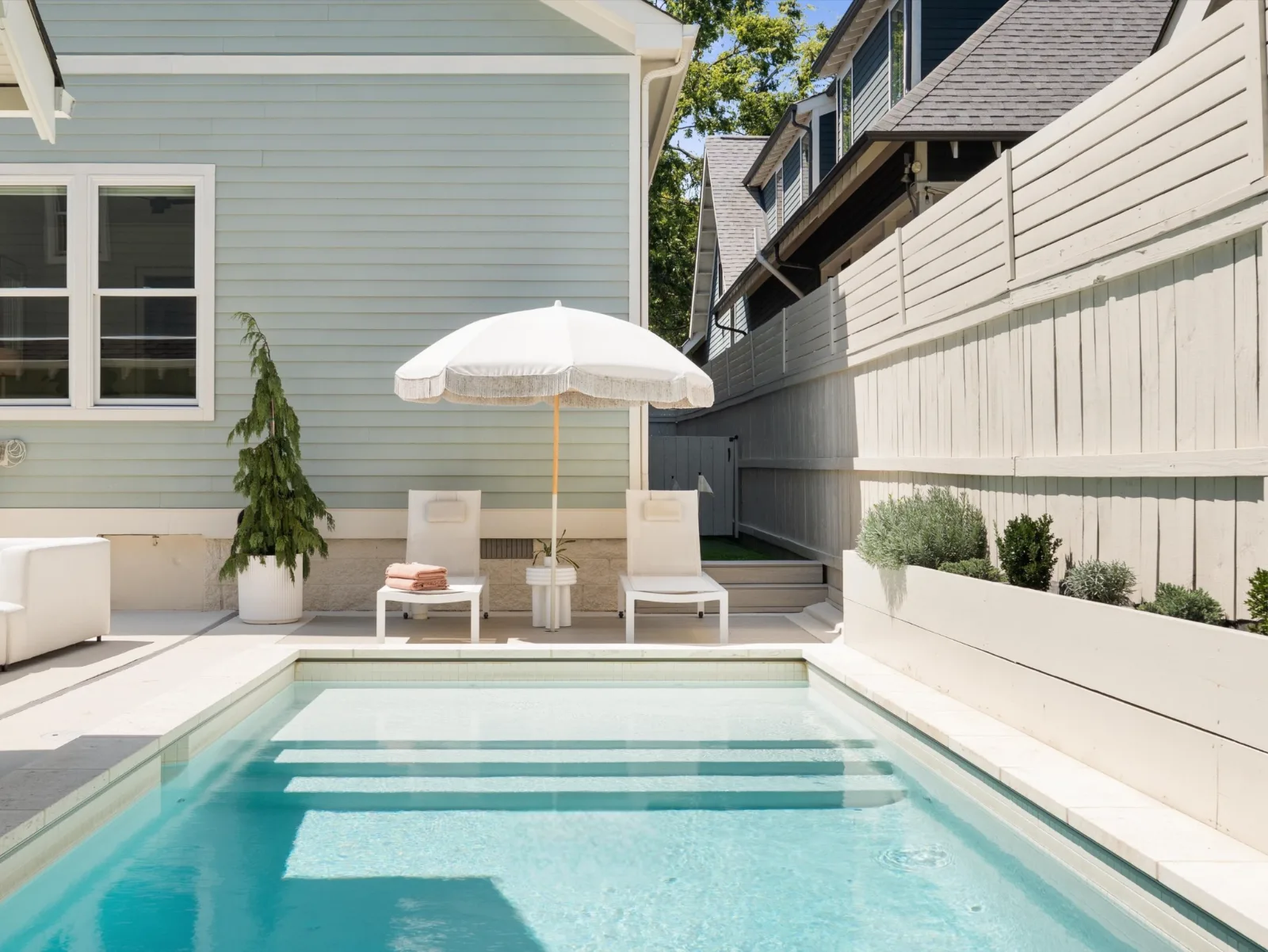 The saltwater pool from the far end, tiled steps running its width, loungers and a fringed umbrella against the siding