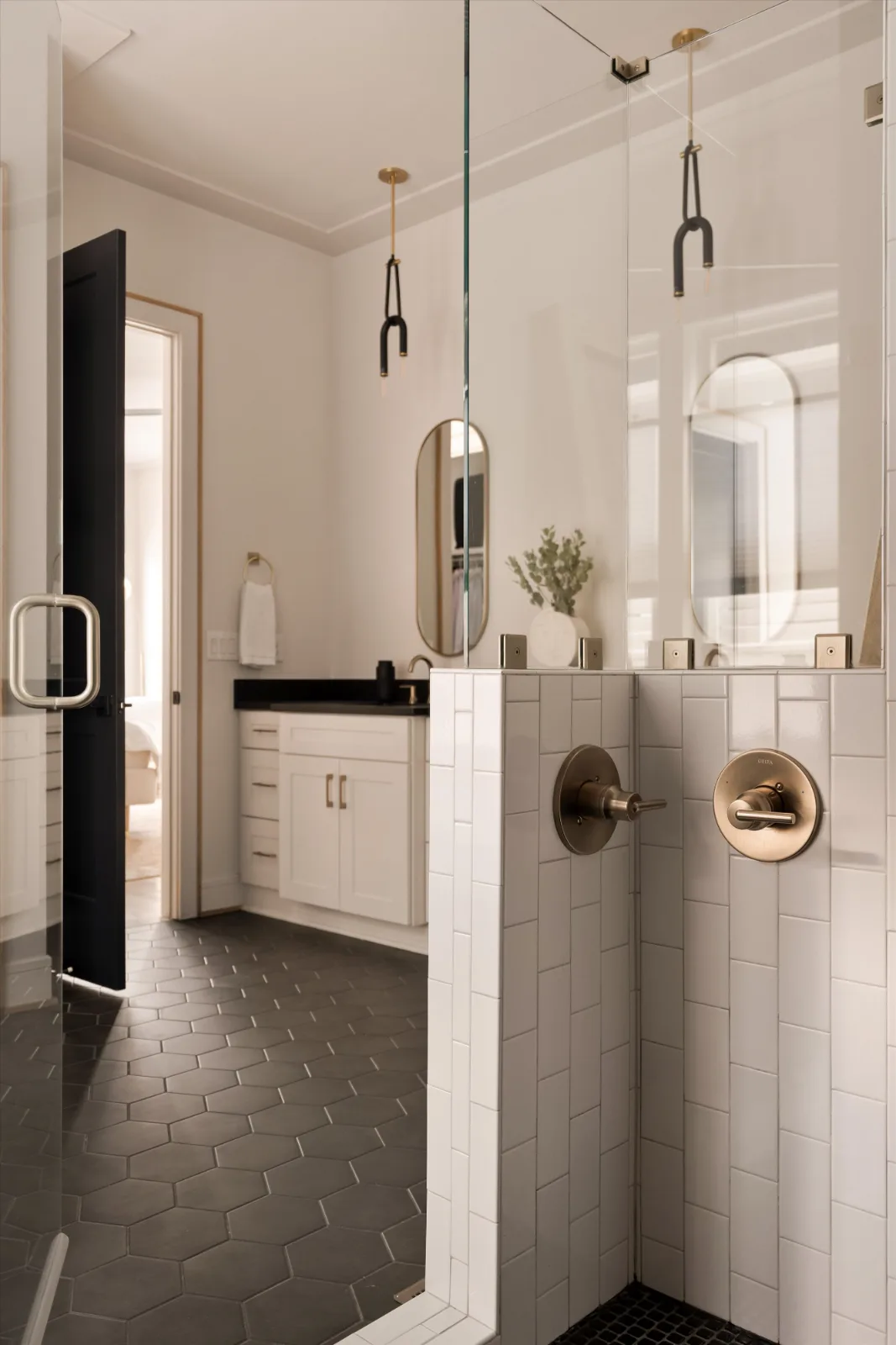 From inside the primary shower: brass valves on white tile, the vanity and the bedroom door beyond