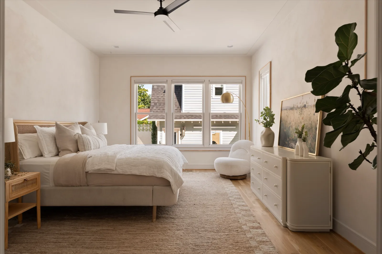 The primary bedroom: cane bed, plaster walls, a run of windows and a swivel chair by the dresser